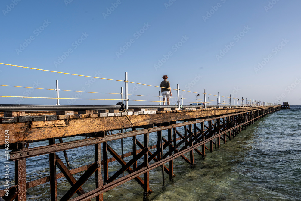 a woman walks along a long bridge over a coral reef into the sea