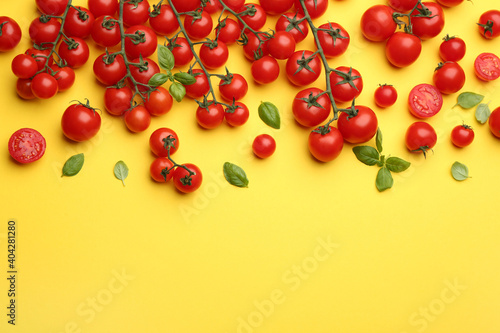 Fresh cherry tomatoes and basil leaves on yellow background, flat lay. Space for text