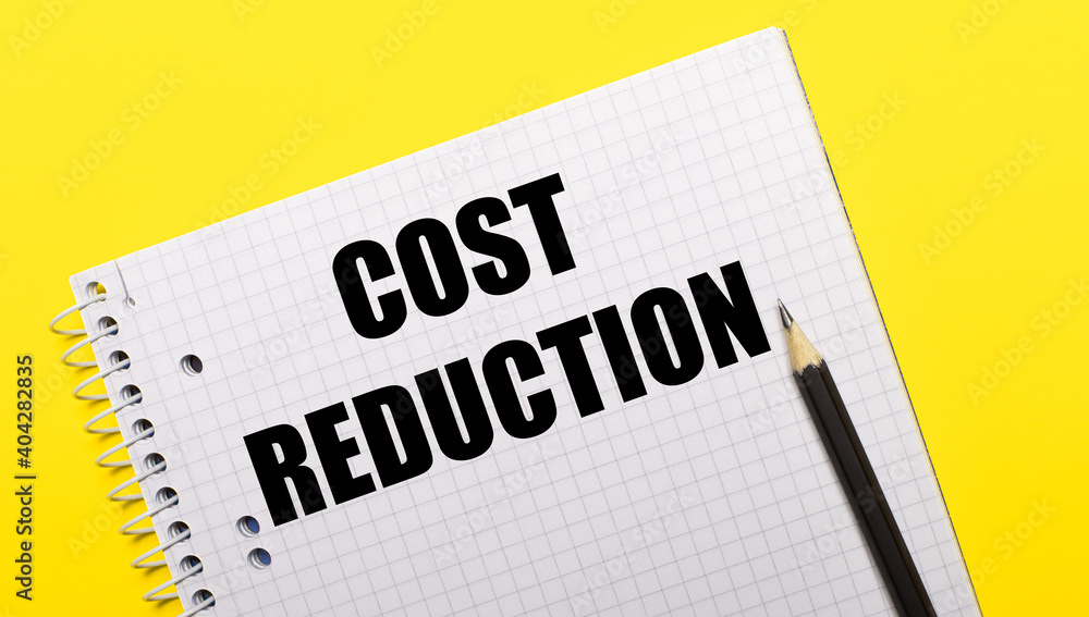 White notebook with COST REDUCTION written in black pencil on a bright yellow background. White notebook with COST REDUCTION written in black pencil on a bright yellow background.
