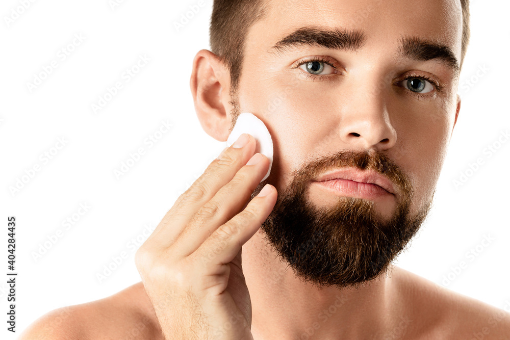 Young handsome man is cleaning his face with a cotton pad