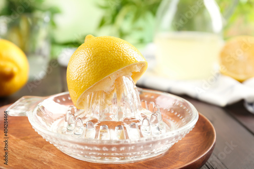 Fotografie Glass citrus squeezer with lemon half on wooden plate