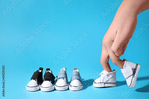 Woman with walking fingers wearing toy canvas shoes on light blue background, closeup photo