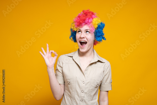 A young female clown shows a gesture OK against a colored background. It's a fool's day.