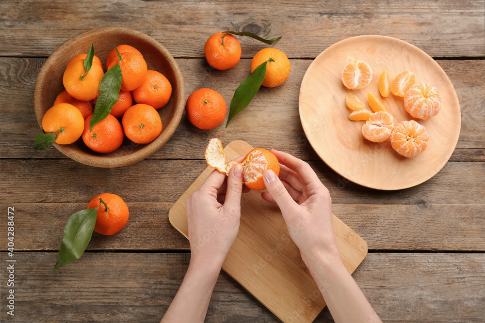 Woman peeling fresh ripe tangerine at wooden table, top view