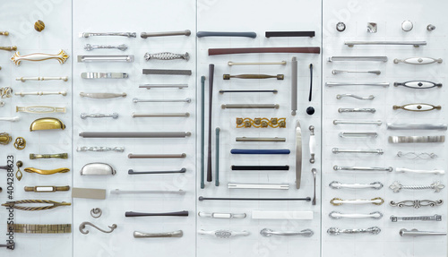 Big selection of handles cabinets parts on a white background shop window. samples of Metal and Stainless Steel handle styles on wooden kitchen cabinet with different Stainless Steel handles.