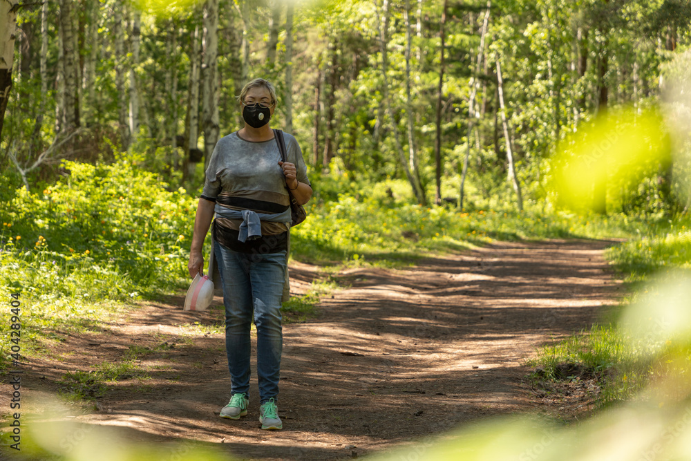 Middle-aged woman in a protective mask walks in the park