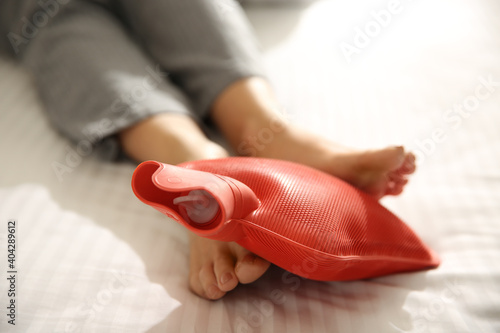 Woman warming feet with hot water bottle on bed  closeup