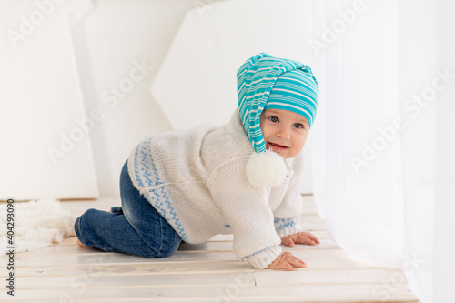 a small child six months old in a knitted warm jacket and hat is crawling at home in a bright room