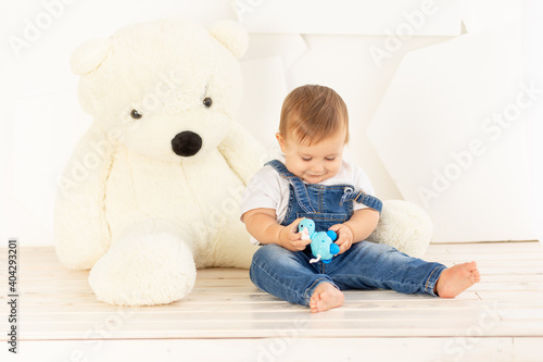 a small child six months old in blue jeans plays at home near a large Teddy bear