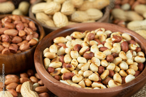 Roasted, raw peanuts and shelled in wooden bowls on a brown wooden table. Peanuts closeup