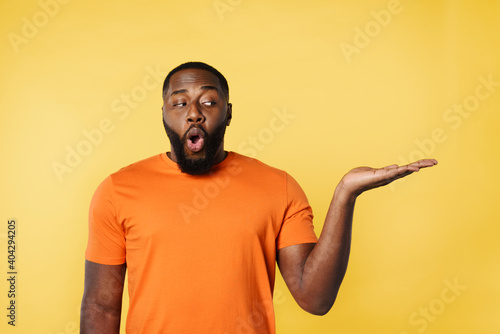 Surprised black man holds something in hand. Yellow background