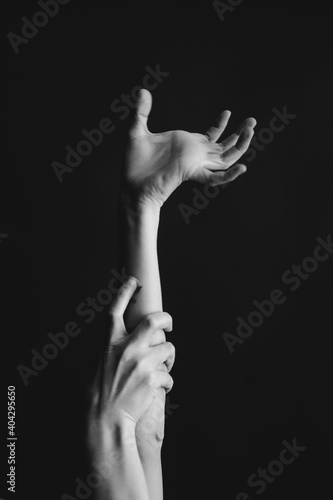Black and white photo of body parts. two hands reach up against the dark background, strong fingers gripping the wrist