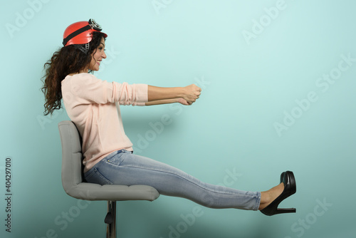 Woman with red helmet thinks to drive a fast car. cyan background.