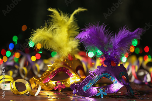 Beautiful carnival masks and party decor on table against blurred lights
