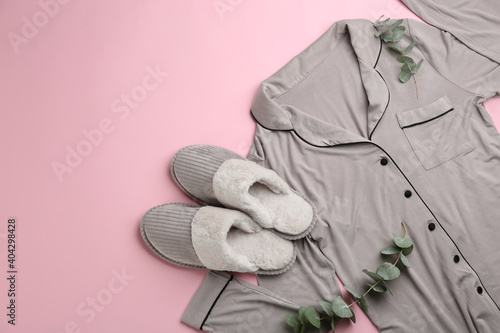 Pair of slippers, pajamas and eucalyptus branches on pink background, flat lay. Comfortable home outfit photo
