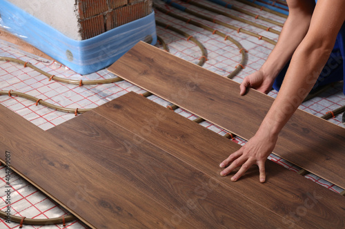 Tablou pe pânză Worker installing new wooden laminate over underfloor heating system, closeup