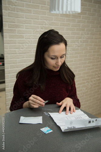 A white girl makes a rapid test for antibodies to coronavirus Ig G and Ig M at home. She opened the test and laid out the tools on the table.