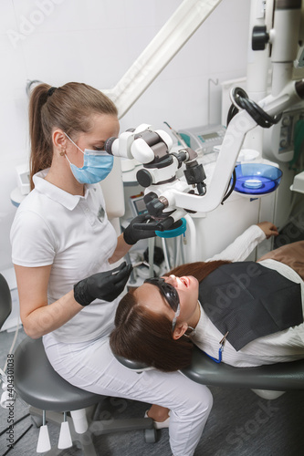 Professional dentist wearing medical face mask  using dental microscope on patient