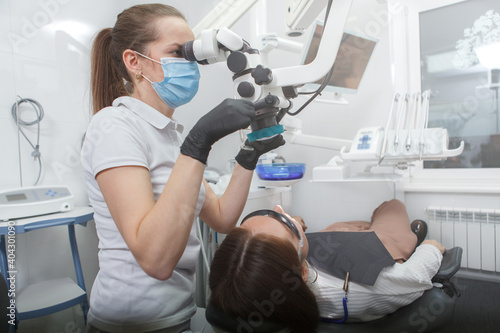Female dentist operating dental microscope  treating teeth of patient