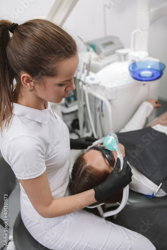 Vertical shot of a professional dentist putting on inhalation sedation mask on her patient