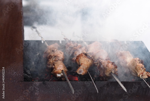 Pieces of chicken fried on skewers, fried over an open fire in winter. Smoke from fire and steam from hot meat in the cold.Blurred image.