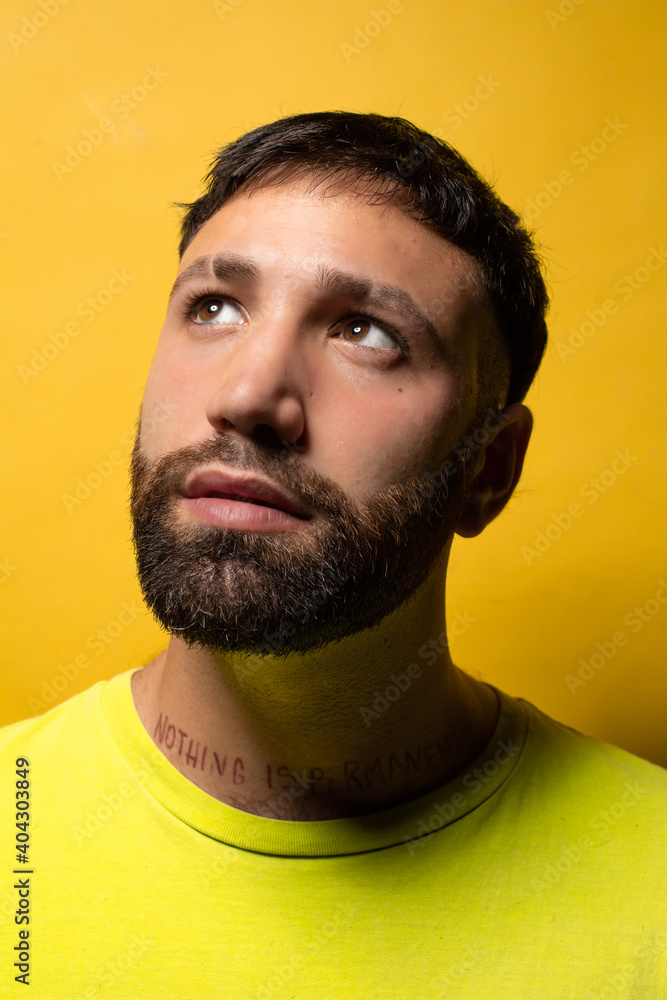 Portrait of smiling young man with beard and yellow t-shirt on yellow background looking up Portrait of smiling young man with beard and yellow t-shirt on yellow background looking up