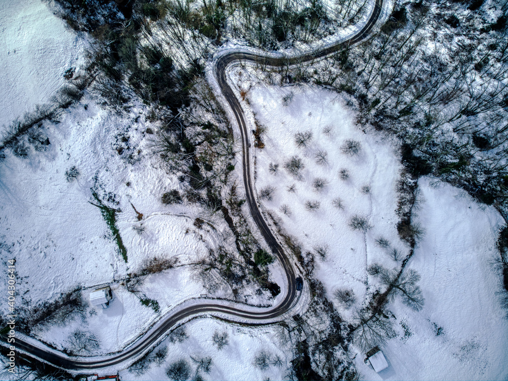 Drone overhead shot of curved road in winter mountain landscape.