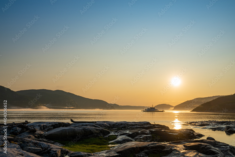Ferry passing across Saguenay river in Tadoussac during sunset with a nice fog in background and birds in foreground