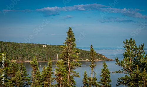 Rocks with forest goes to a huge river in Quebec, Canada, with trees in the foreground at golden hour during the summer