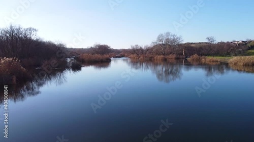 
Drone flight above calm blue water surface of river Southern Bug with rising higher overlooking at green shore, river rapids and leafless trees at winter in Ukraine photo