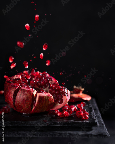 Freeze motion of sliced pomegranate red fruit with splashing juice, drops and seeds on black background. Copy space.