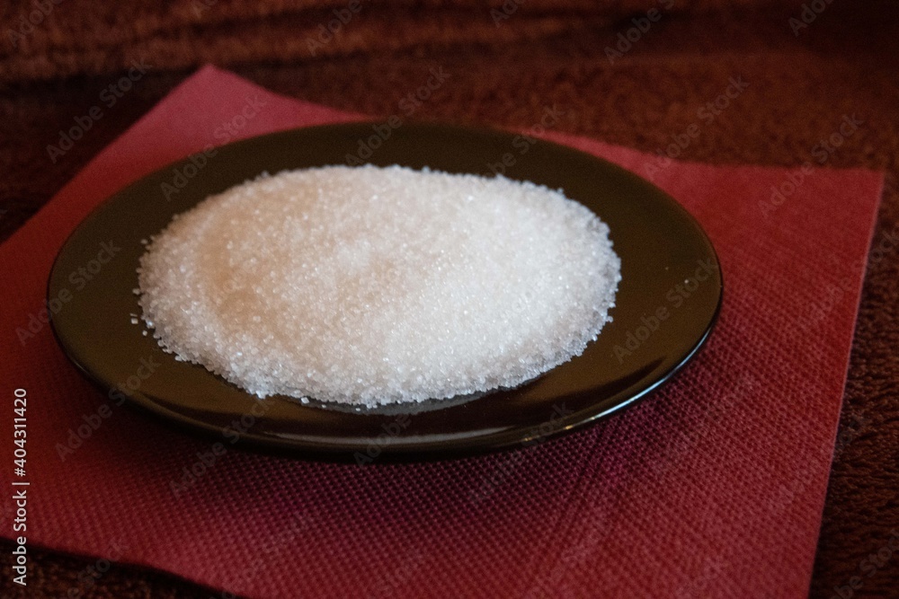 Black plate with sugar on brown tablecloth Black plate with sugar on brown tablecloth