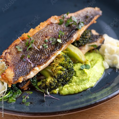 Grilled sea bass with broccoli and pea puree on a wooden table photo