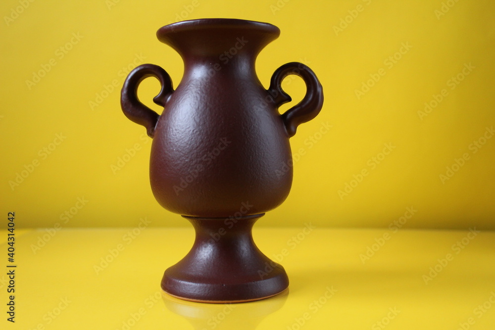 brown amphora vase with handles on a yellow background copyspace