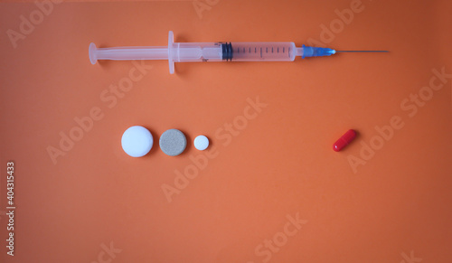 Medical syringe with needle and tablets on an orange background. Multi-colored tablets on a colored background.