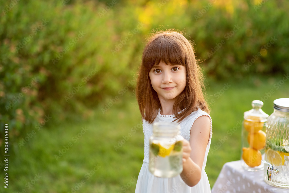 Girl in the summer makes homemade lemonade. Detox fruit infused flavored water, cocktail in a beverage dispenser with fresh fruits Girl in the summer makes homemade lemonade. Detox fruit infused flavored water, cocktail in a beverage dispenser with fresh fruits