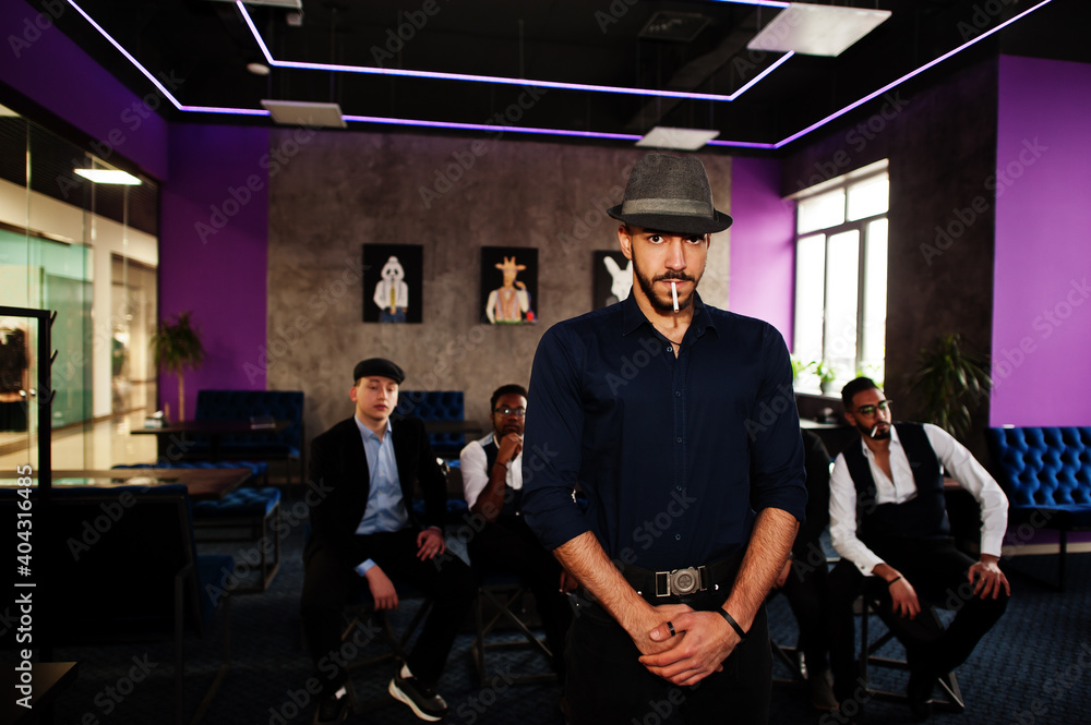 Obraz premium Stylish arab man in hat against group of handsome retro well-dressed guys gangsters spend time at club. Multiethnic male bachelor mafia party in restaurant.
