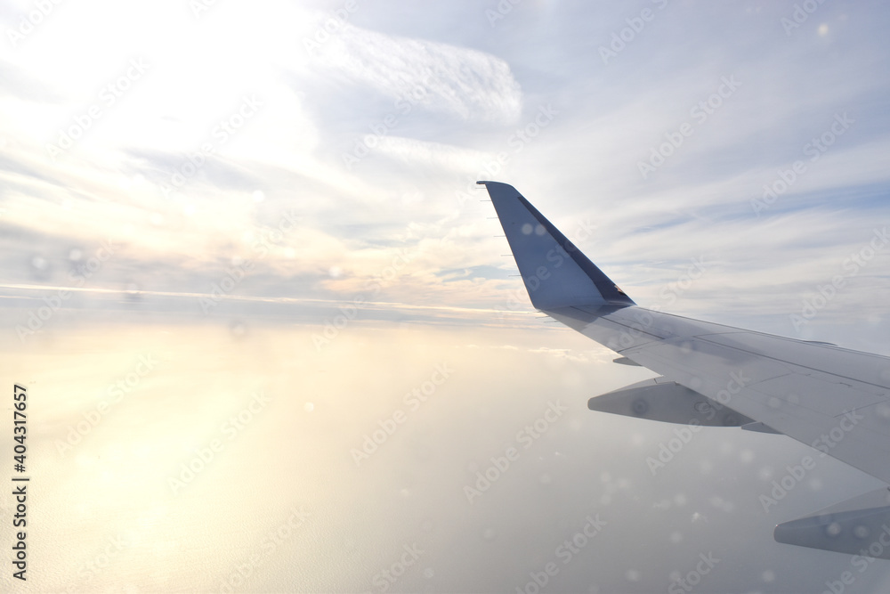 Obraz premium Airplane wing flying above white clouds obscure light from the sun. View from aircraft window