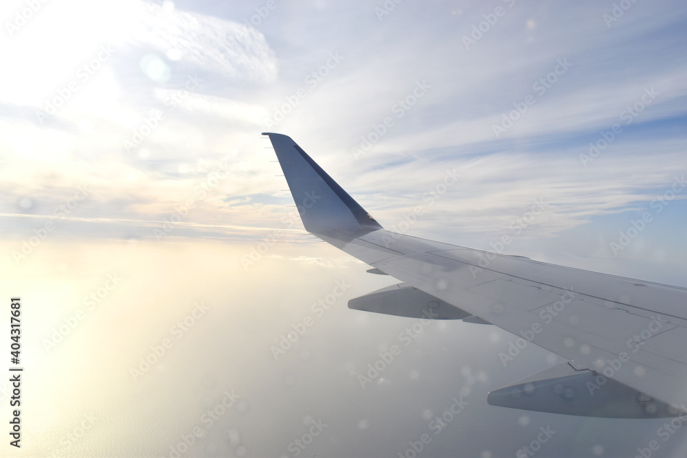 Fototapeta premium Airplane wing flying above white clouds obscure light from the sun. View from aircraft window
