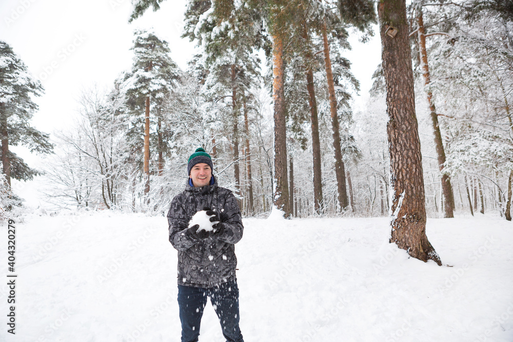 A young man with a snowball in his hand is having fun, swinging for a throw. Winter family and friendly games and entertainment in the forest with snow in the open air