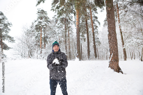 A young man with a snowball in his hand is having fun, swinging for a throw. Winter family and friendly games and entertainment in the forest with snow in the open air