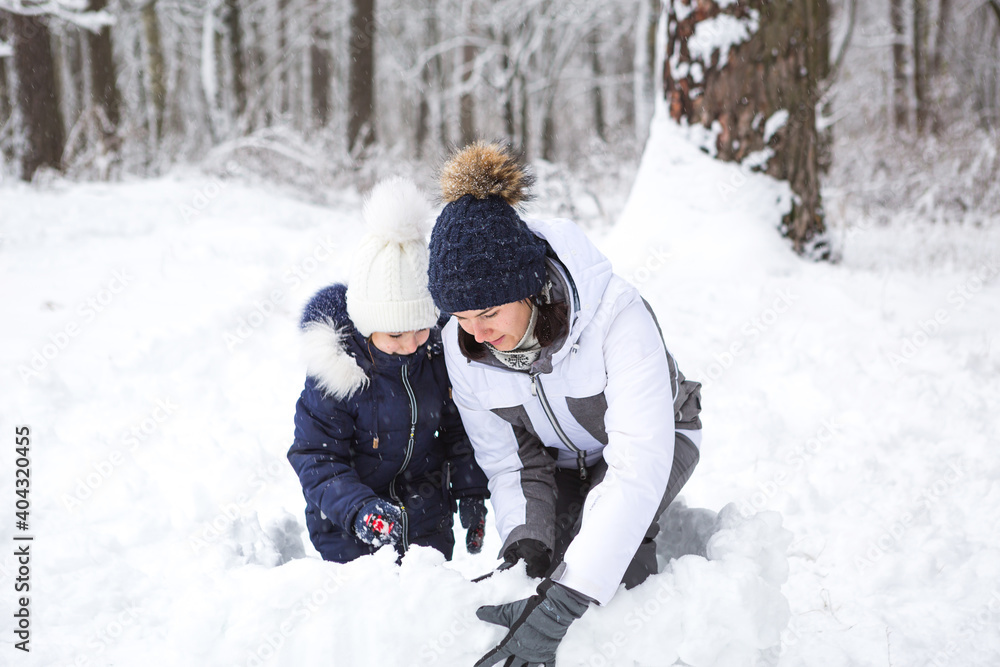 Mom and daughter play snow games, build a fortress, make snowballs. Winter entertainment outside, active recreation, fun in the cold in warm clothes. Outdoor recreation, fun childhood, strong family