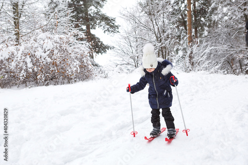 Children's feet in red plastic skis with sticks go through the snow from a slide-a winter sport, family entertainment in the open air. A little girl glides down the slope from an early age. Copy space