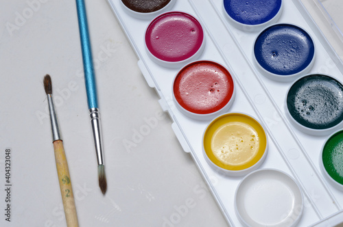 multicolored paints for drawing in a palette and a brush. on a light background close-up.