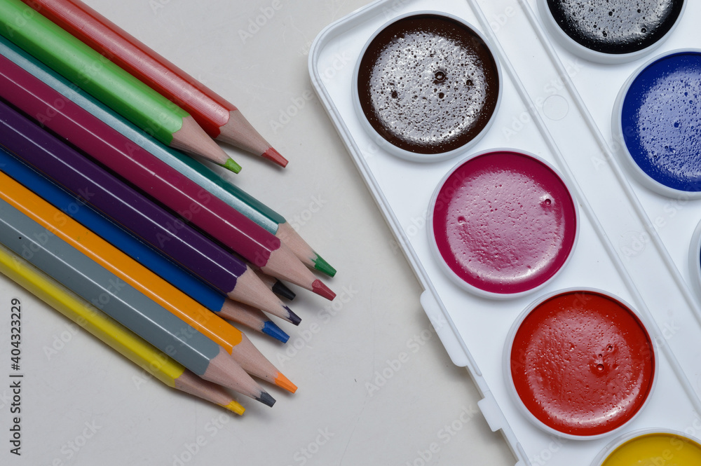 Naklejka premium multi-colored paints for drawing in a palette, a brush and pencils on a light background. close-up.