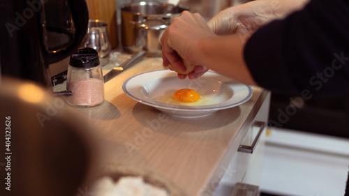 Close up shot of Caucasian woman cracking an egg in white plate. Housewife preparing breakfast in kitchen.