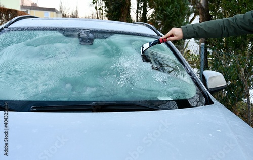 Man cleans the windshield of ice with ice scraper. 