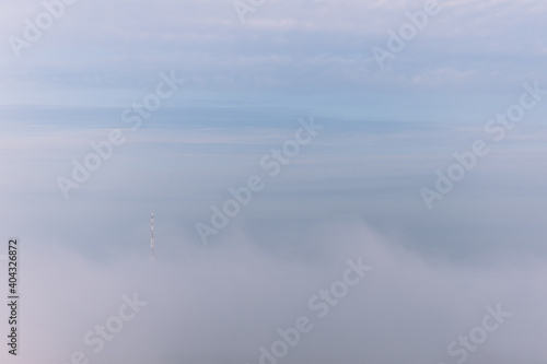Silhouette of high television or electric tower seen slighty among thick clouds of morning fog and mist. Unusual morning panorama of dramatic landscape.