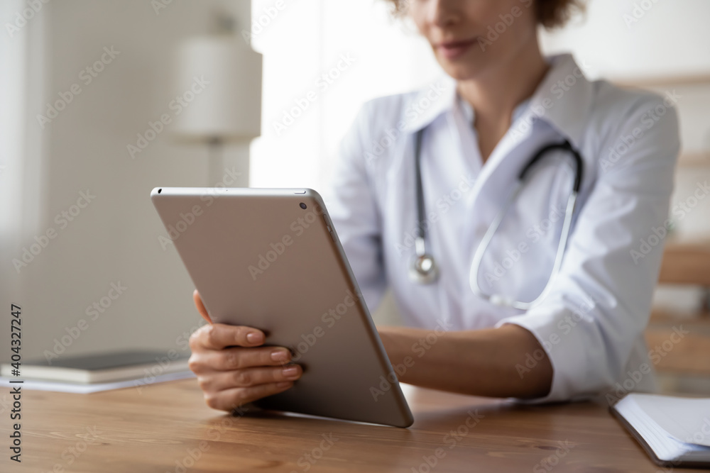 Close up young female general practitioner using digital computer tablet at clinic office., web surfing medical information or managing appointments, medical service and modern technology concept. Close up young female general practitioner using digital computer tablet at clinic office., web surfing medical information or managing appointments, medical service and modern technology concept.