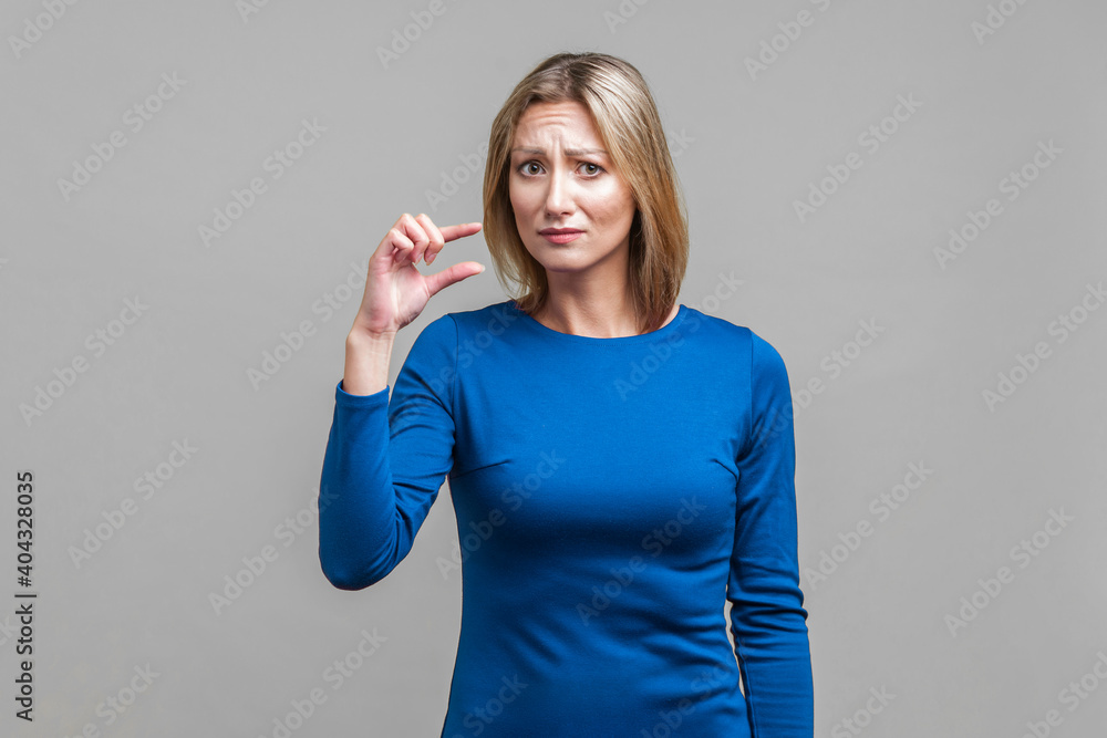 Φωτογραφία Portrait of disappointed woman in elegant blue dress frowning and showing a little bit gesture, asking some more, dissatisfied upset with amount